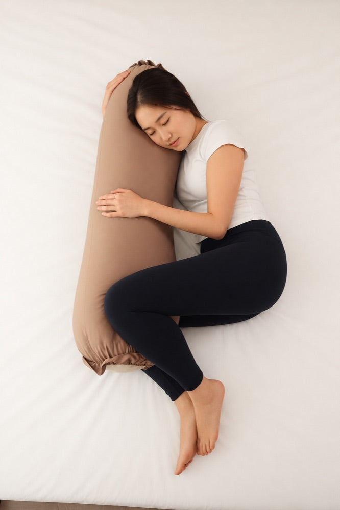 Woman sleeping on her side hugging a tan Koalu body pillow, seen from above